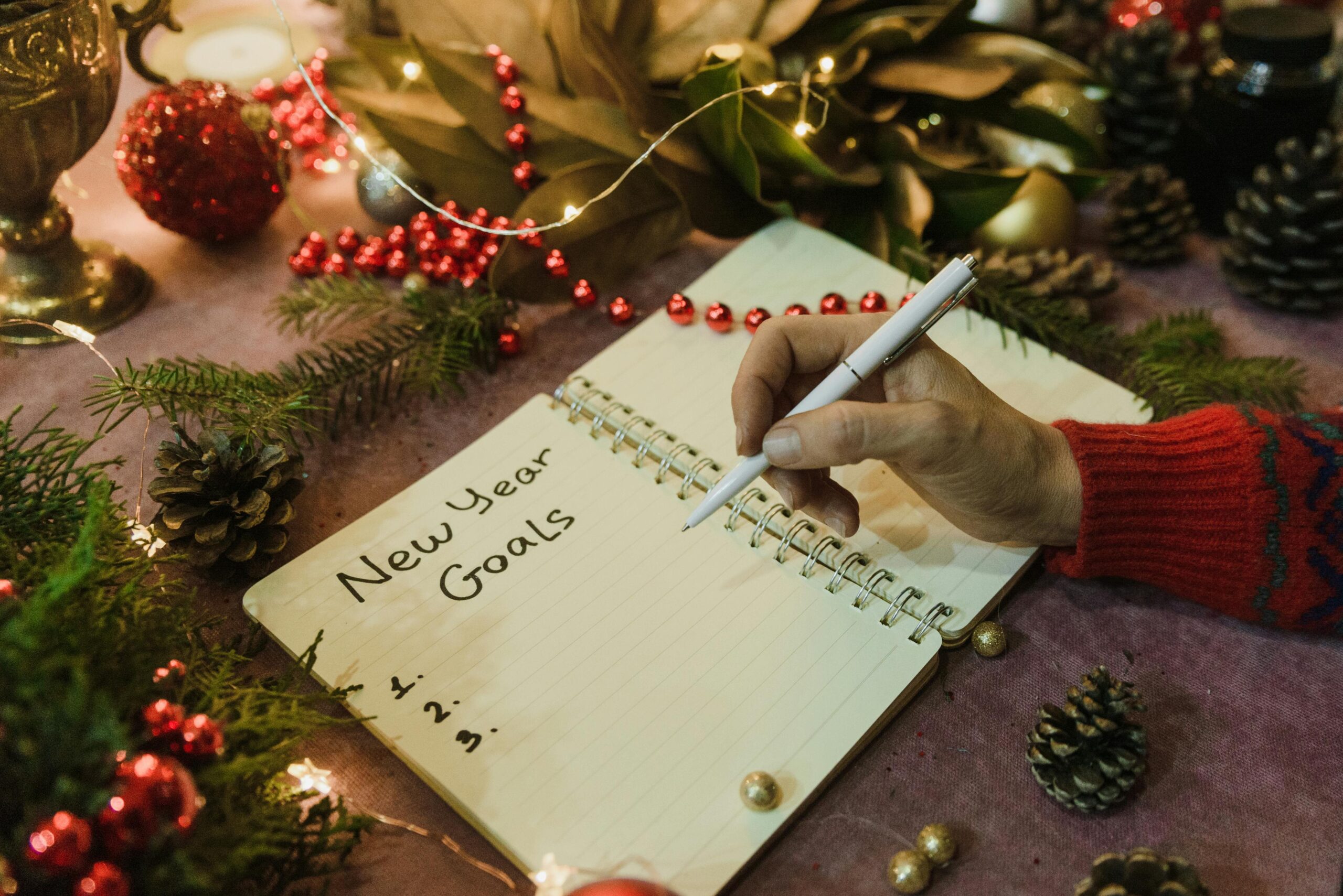 A person writing New Year goals in a decorated holiday setting with Christmas elements.