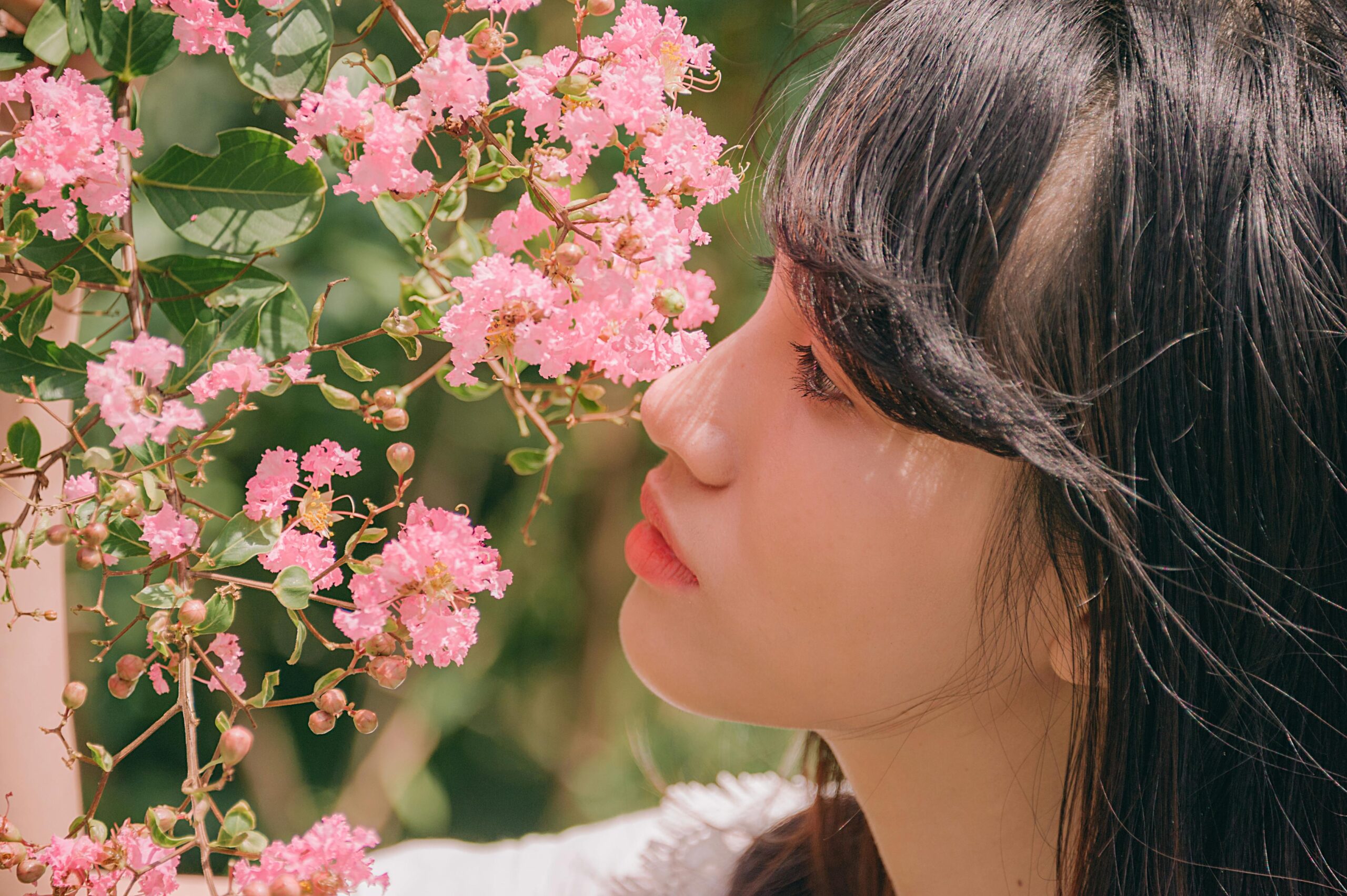 Asian woman enjoying the scent of vibrant pink blossoms outdoors.
